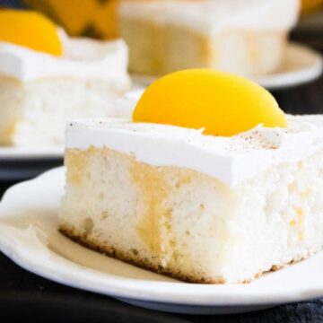 Slice of Summer Peach Pie Poke Cake with whipped topping and a peach slice on a white plate